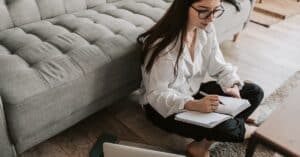 woman sitting on floor with notebook and computer getting paid writing