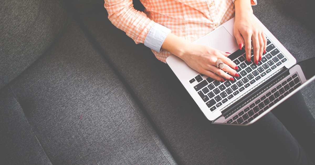 woman writing a blog on a laptop on a couch freelance writer