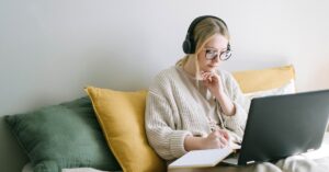 woman working as freelance writer sitting on couch with computer notebook and headphones