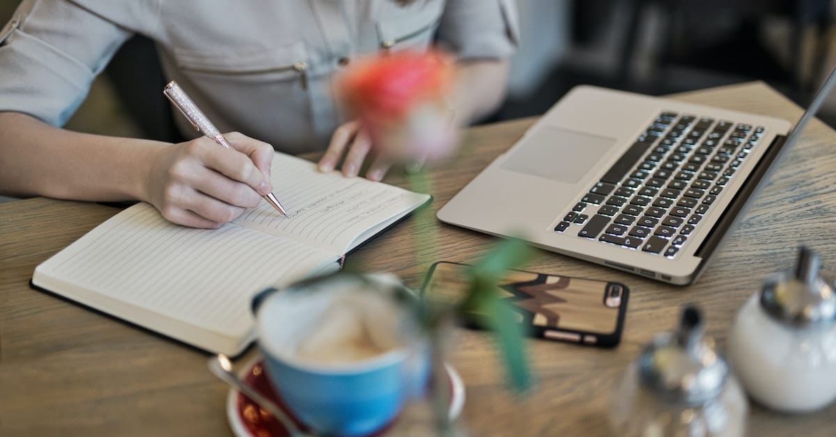 woman writing in notebook with flower and laptop after reading writer quotes for inspiration